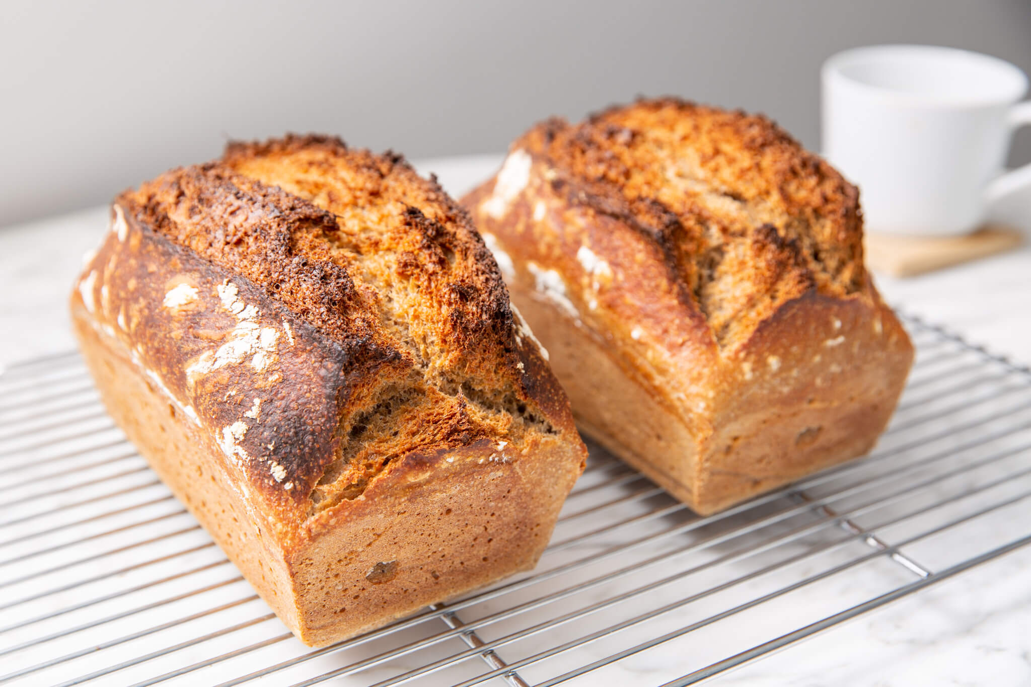 2 loaves of whole wheat sourdough sandwich bread cooling on a wire wrack