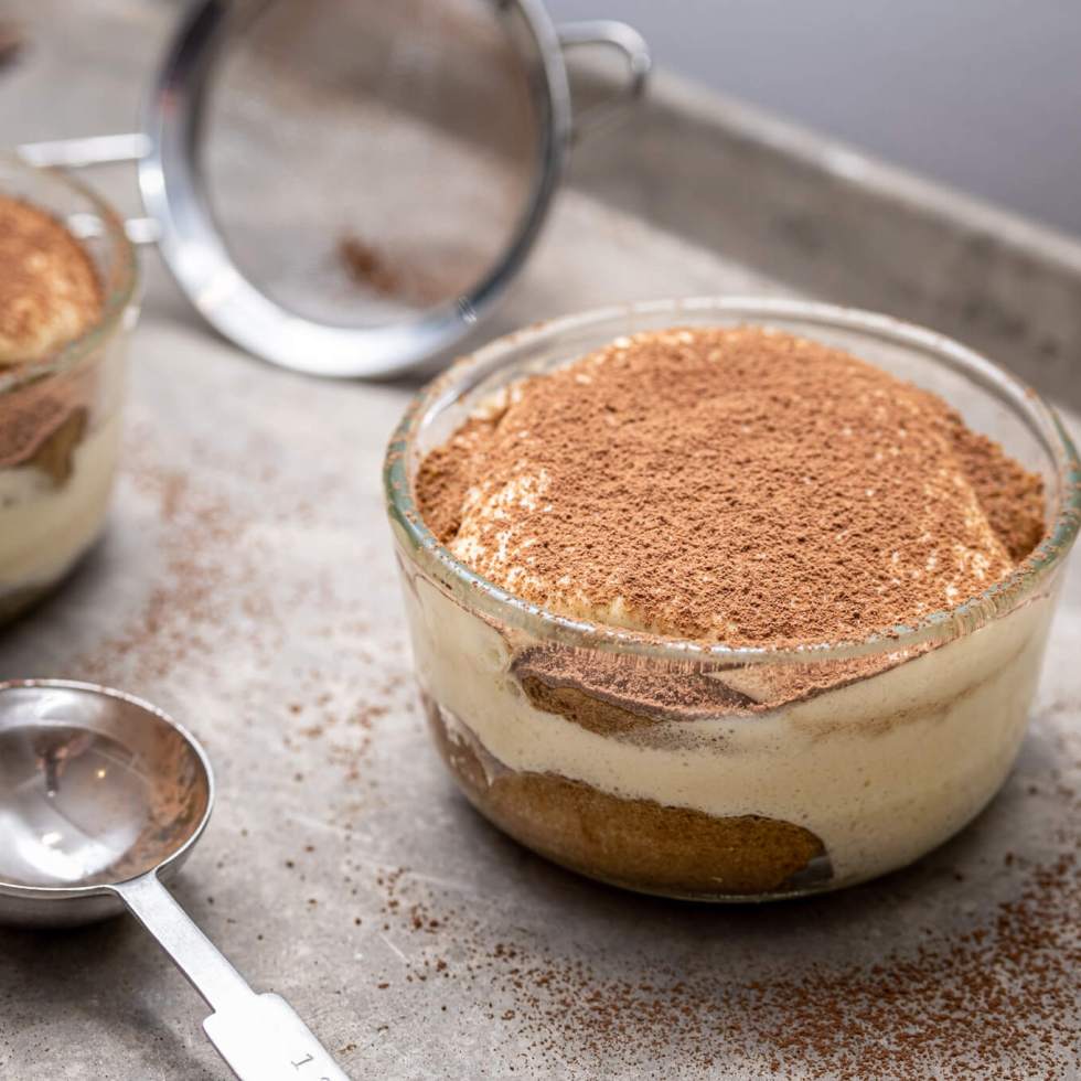 Tiramisú in a glass ramekin dusted with cocoa powder