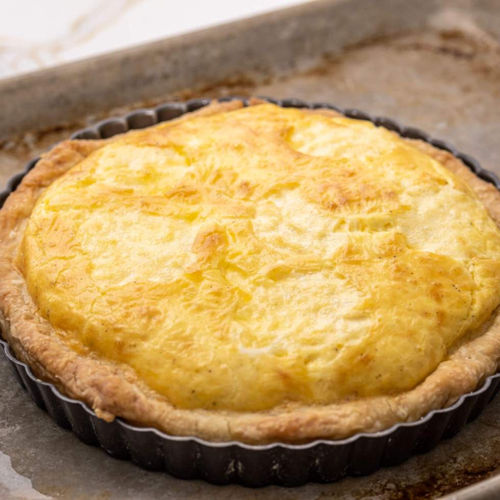 A whole cheese quiche in a tart pan on a baking sheet