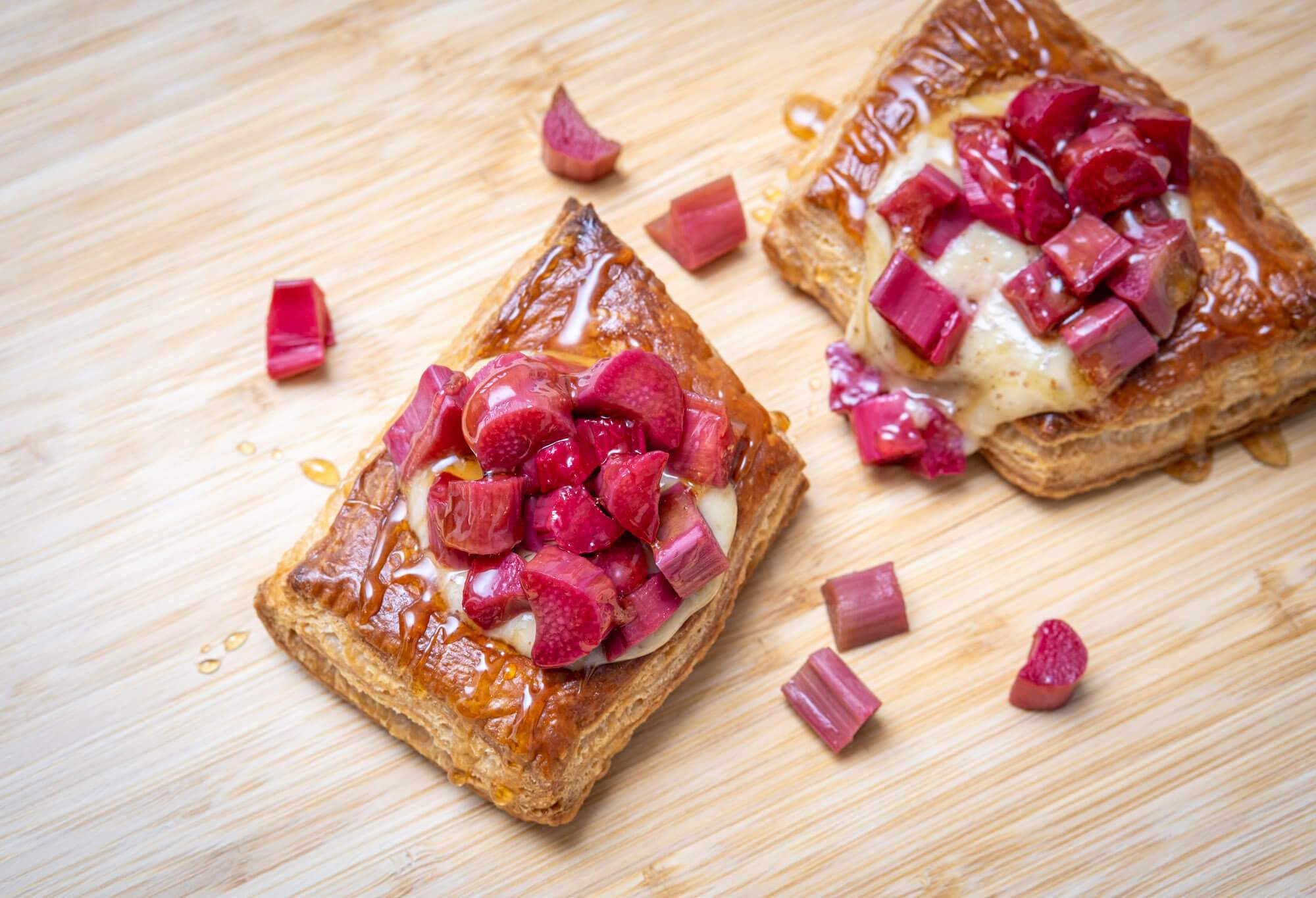 Two puff pastry tarts with almond pastry cream and pieces of poached rhubarb, on a bamboo cutting board